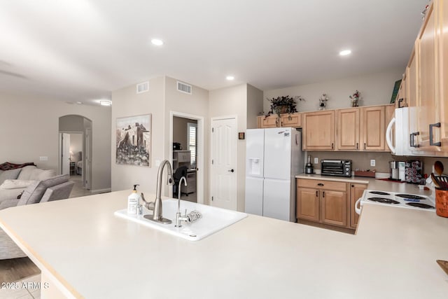 kitchen with kitchen peninsula, light brown cabinetry, white appliances, and sink