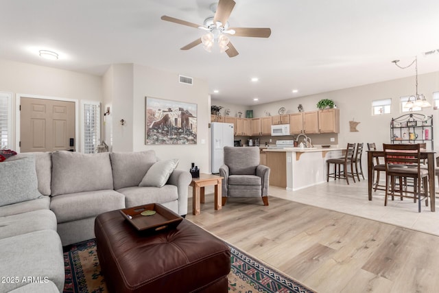 living room featuring ceiling fan with notable chandelier, light wood-type flooring, and sink