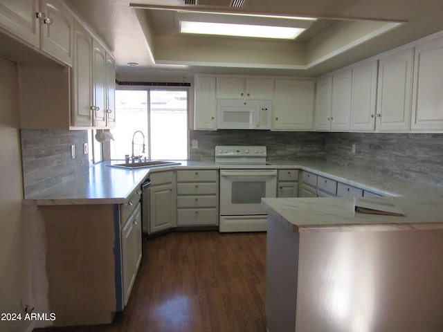 kitchen featuring kitchen peninsula, white appliances, a tray ceiling, sink, and white cabinets