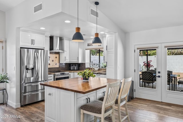 kitchen featuring dark wood finished floors, butcher block counters, stainless steel appliances, visible vents, and wall chimney exhaust hood