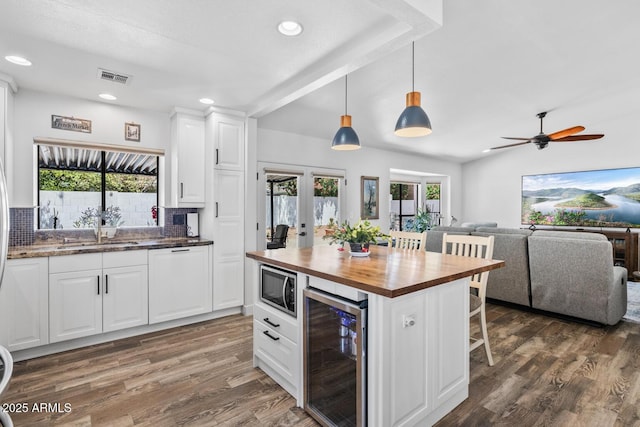 kitchen featuring stainless steel microwave, a sink, beverage cooler, visible vents, and wooden counters