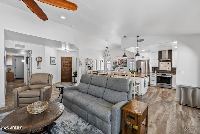 living room featuring visible vents, a ceiling fan, light wood-style floors, and vaulted ceiling