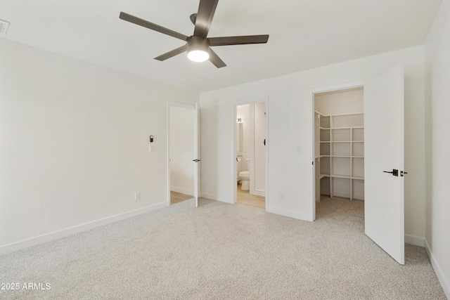 unfurnished bedroom featuring a walk in closet, baseboards, light colored carpet, and a closet