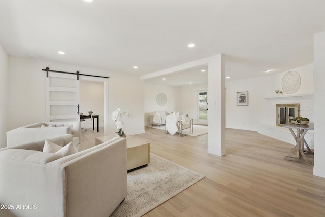 living room with recessed lighting, light wood-type flooring, a barn door, and a fireplace