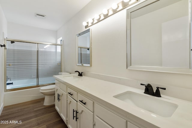 bathroom featuring toilet, shower / bath combination with glass door, wood finished floors, and a sink