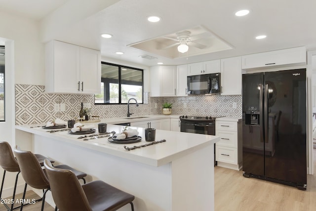 kitchen featuring black appliances, a sink, a breakfast bar area, a raised ceiling, and ceiling fan