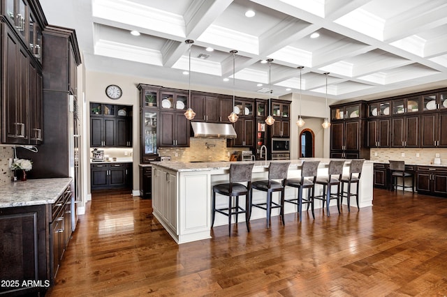 kitchen with a kitchen breakfast bar, hanging light fixtures, a large island, dark brown cabinetry, and light stone countertops