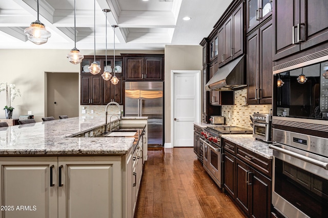 kitchen with dark hardwood / wood-style floors, pendant lighting, sink, built in appliances, and dark brown cabinetry