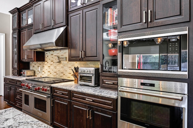 kitchen with light stone counters, dark brown cabinets, stainless steel appliances, and decorative backsplash