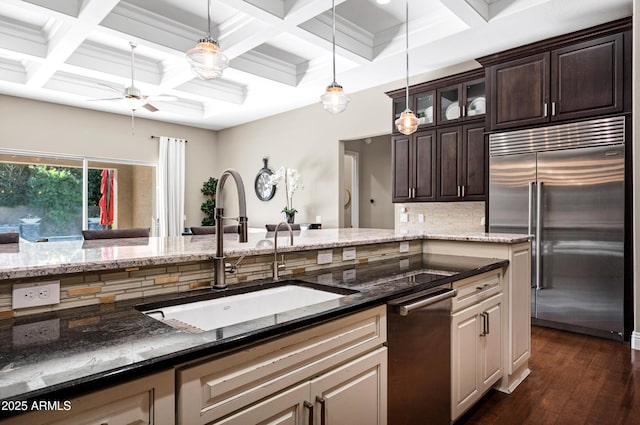 kitchen with dark brown cabinetry, sink, built in fridge, and dark stone countertops