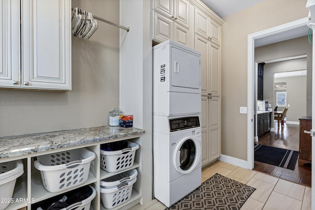 washroom featuring cabinets, stacked washing maching and dryer, and light wood-type flooring