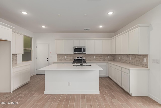 kitchen with light countertops, appliances with stainless steel finishes, an island with sink, and white cabinets