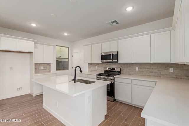 kitchen featuring appliances with stainless steel finishes, white cabinetry, a sink, and an island with sink