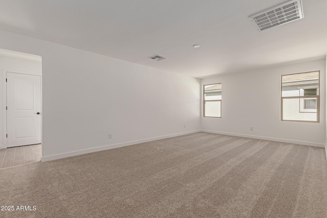 empty room featuring baseboards, visible vents, and light colored carpet