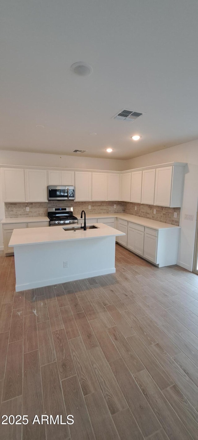 kitchen with light countertops, a center island with sink, white cabinetry, and stainless steel appliances