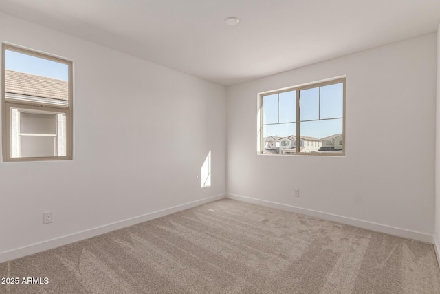 spare room featuring plenty of natural light, baseboards, and light colored carpet