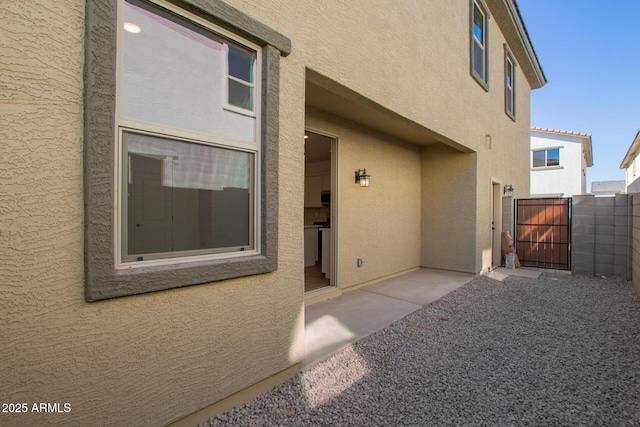 entrance to property featuring a patio area, a gate, fence, and stucco siding