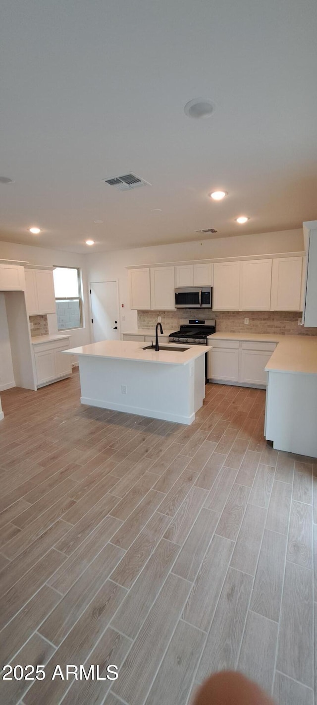 kitchen with white cabinets, light countertops, appliances with stainless steel finishes, decorative backsplash, and an island with sink