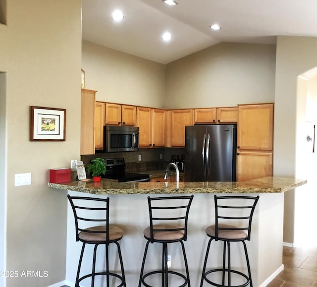 kitchen featuring light stone counters, a kitchen breakfast bar, kitchen peninsula, backsplash, and appliances with stainless steel finishes