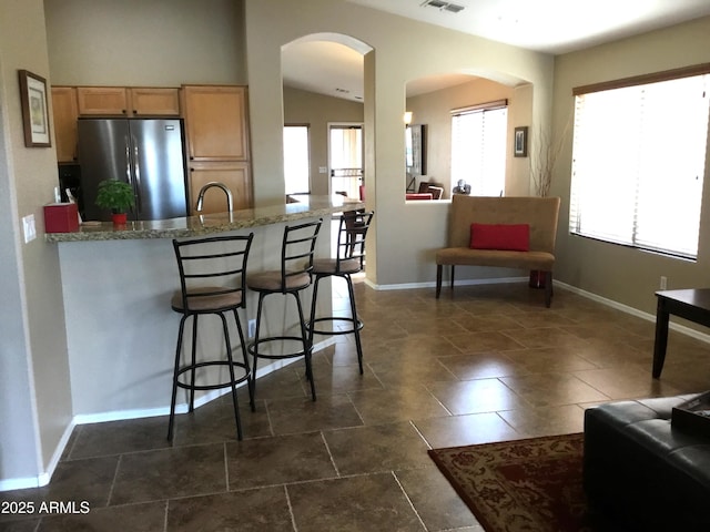 kitchen featuring lofted ceiling, light stone countertops, stainless steel fridge, and a breakfast bar