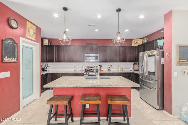 kitchen with decorative light fixtures, a kitchen breakfast bar, an island with sink, and appliances with stainless steel finishes