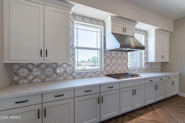 kitchen featuring under cabinet range hood, stainless steel gas cooktop, white cabinets, light countertops, and decorative backsplash