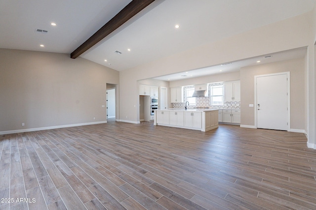 unfurnished living room with light wood-type flooring, vaulted ceiling with beams, and baseboards