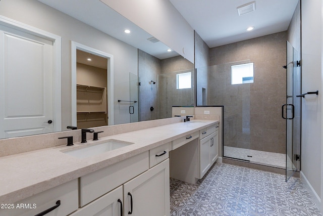 bathroom with a walk in closet, double vanity, visible vents, a stall shower, and a sink