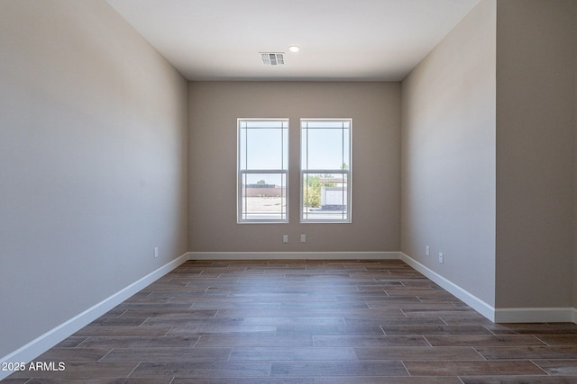 unfurnished room with visible vents, dark wood finished floors, and baseboards