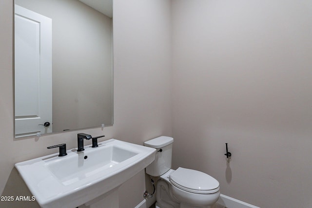 bathroom featuring toilet, baseboards, and a sink