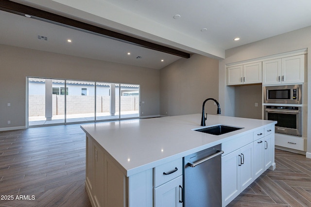 kitchen with appliances with stainless steel finishes, open floor plan, white cabinets, a sink, and beamed ceiling