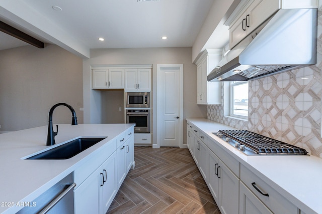 kitchen with under cabinet range hood, stainless steel appliances, a sink, light countertops, and decorative backsplash