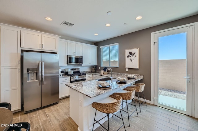 kitchen with white cabinetry, appliances with stainless steel finishes, a kitchen breakfast bar, and wood tiled floor
