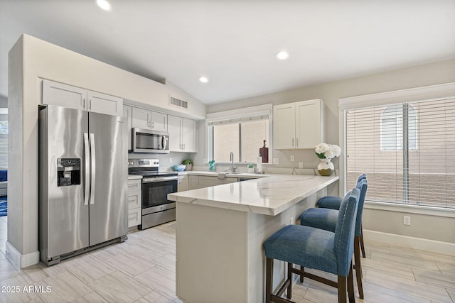 kitchen with white cabinetry, lofted ceiling, a kitchen bar, kitchen peninsula, and stainless steel appliances