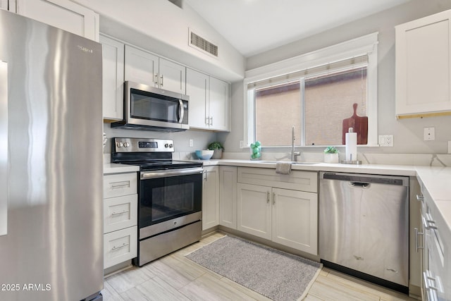 kitchen featuring stainless steel appliances, vaulted ceiling, sink, and white cabinets