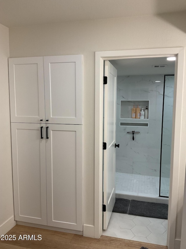 bathroom with a tile shower and wood-type flooring