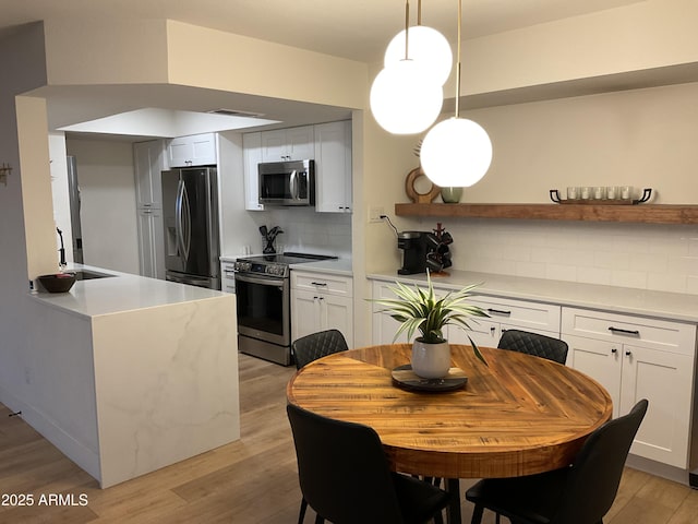 kitchen featuring backsplash, hanging light fixtures, sink, appliances with stainless steel finishes, and white cabinetry