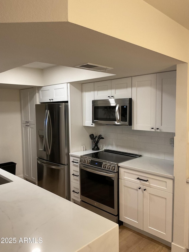 kitchen with light wood-type flooring, backsplash, stainless steel appliances, and white cabinetry