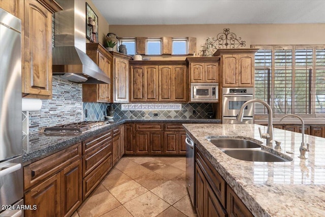 kitchen featuring dark stone countertops, sink, stainless steel appliances, and wall chimney range hood