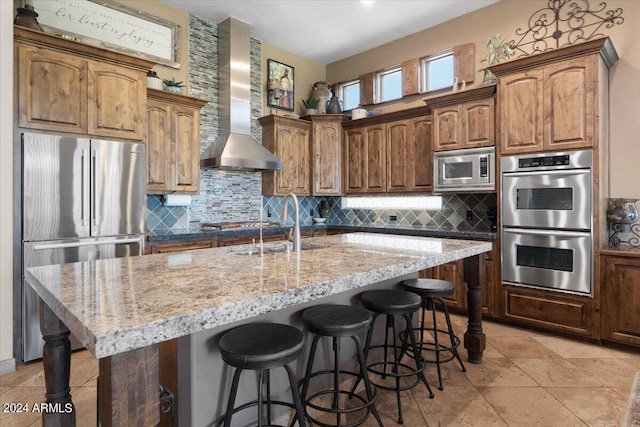 kitchen with appliances with stainless steel finishes, a kitchen island with sink, and wall chimney exhaust hood