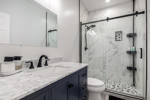 bathroom featuring a shower with door, vanity, and toilet