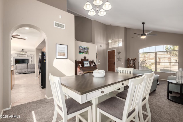 dining area with ceiling fan with notable chandelier, light carpet, and high vaulted ceiling