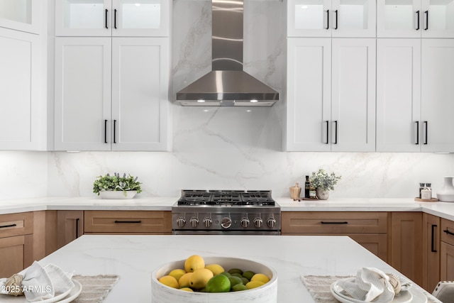 kitchen featuring range, wall chimney range hood, decorative backsplash, glass insert cabinets, and white cabinets