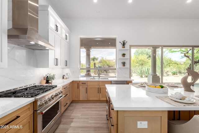 kitchen featuring stainless steel stove, wall chimney exhaust hood, a sink, tasteful backsplash, and light wood-type flooring