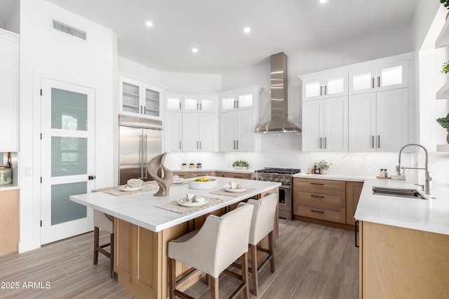 kitchen with premium appliances, wall chimney range hood, a sink, a breakfast bar, and a center island