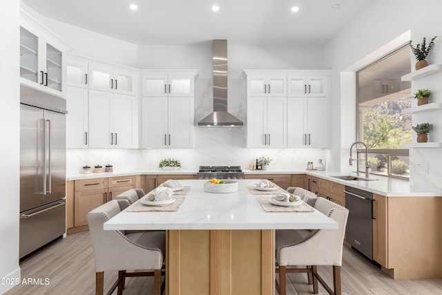 kitchen with appliances with stainless steel finishes, a sink, wall chimney exhaust hood, a breakfast bar area, and recessed lighting