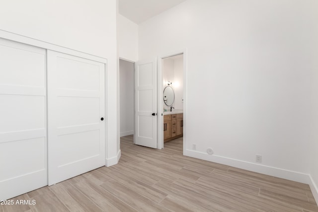 unfurnished bedroom featuring a closet, light wood-type flooring, baseboards, connected bathroom, and a sink