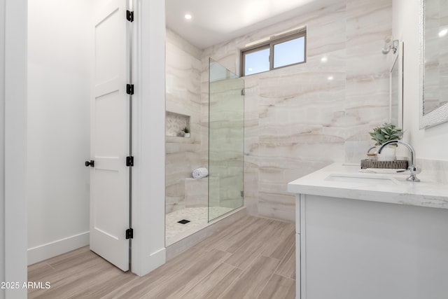 bathroom featuring a marble finish shower, wood finished floors, and vanity