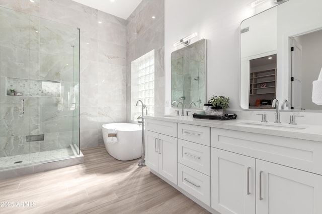 full bath featuring a shower stall, a soaking tub, double vanity, wood finished floors, and tile walls