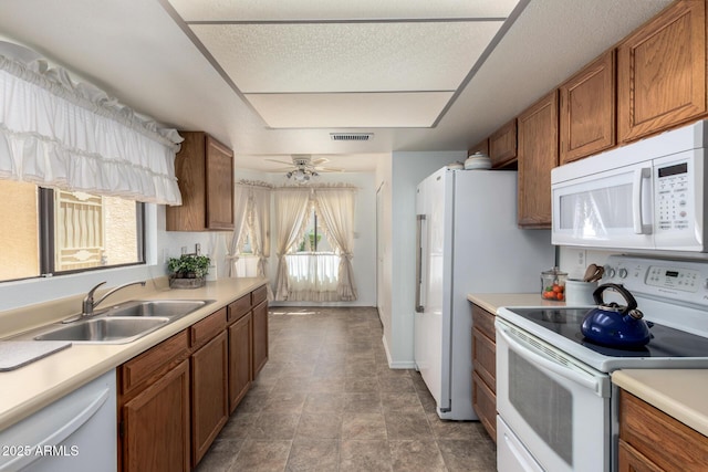 kitchen with a sink, light countertops, brown cabinetry, and white appliances